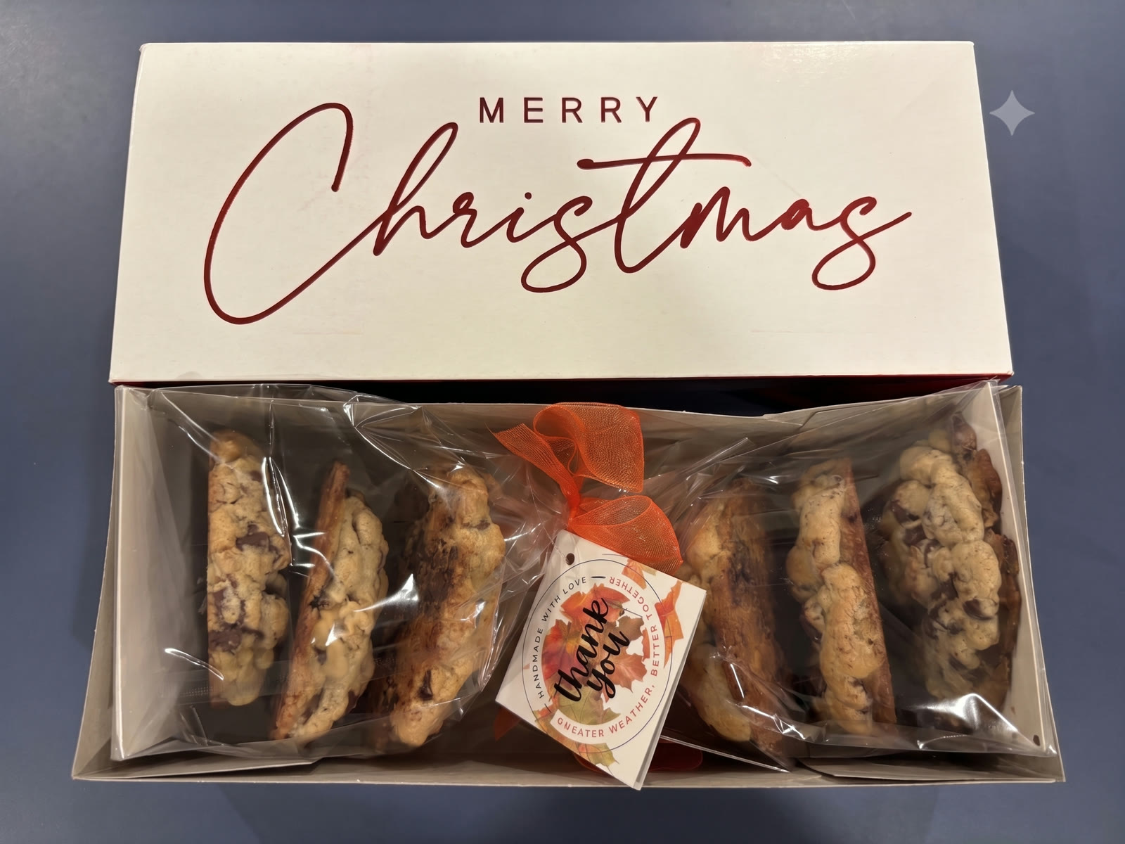 An open Merry Christmas gift box filled with wrapped Teens2Table cookies